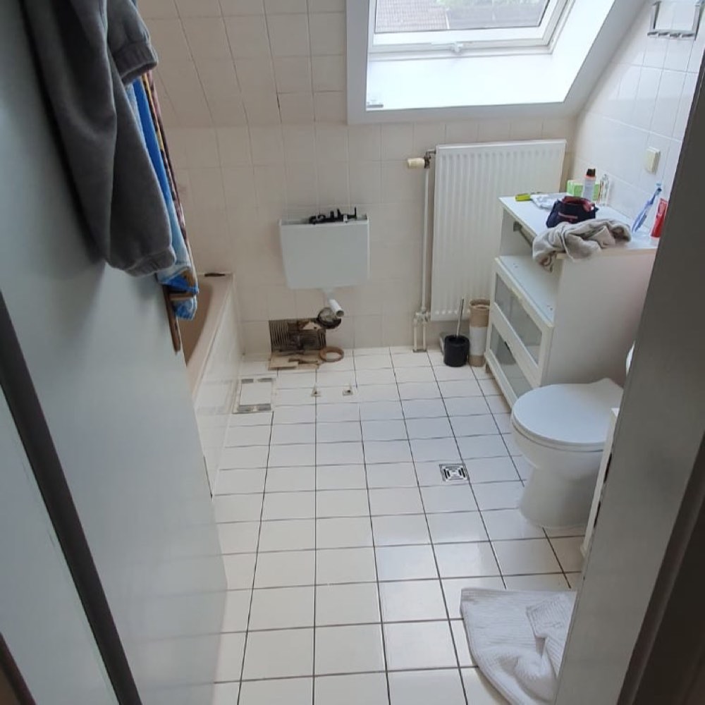 Altes Dachbad mit kleinformatigen weißen Fliesen, demontierter Wanne und freiliegenden Anschlüssen