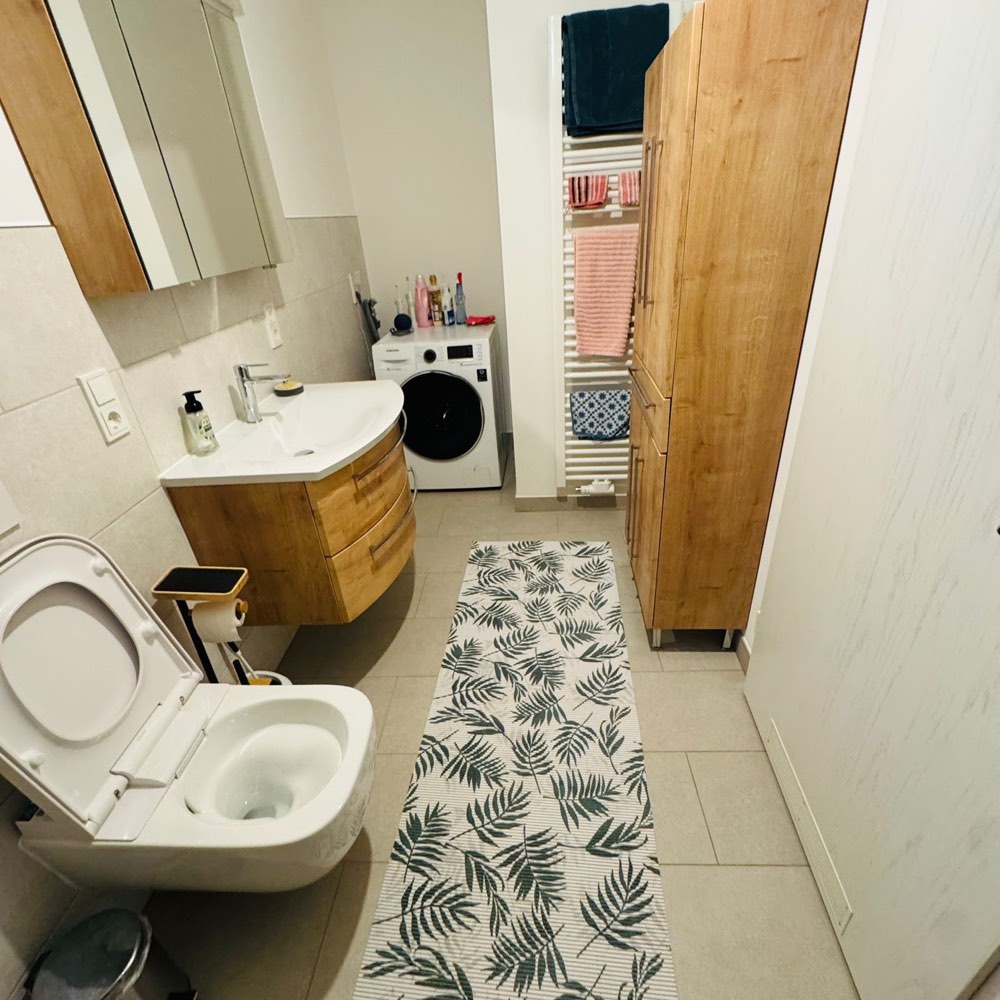 Dasselbe Bad mit hellem Fliesenboden, neuem Waschtisch, Hochschrank und Platz für die Waschmaschine
