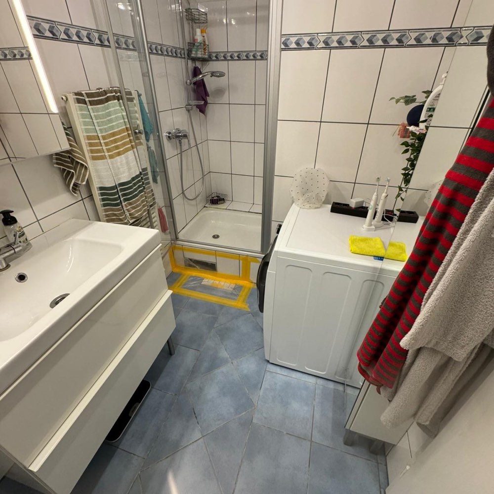 Altes Bad mit Duschkabine, blauem Fliesenboden und abgeklebtem Bodenablauf