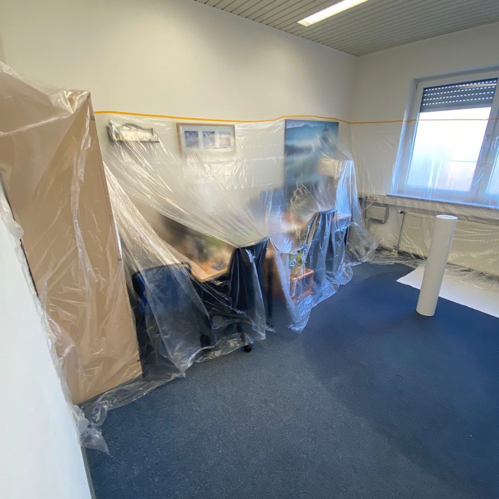 Dasselbe Büro während der Arbeiten: Möbel und Technik mit Folie abgedeckt, Kanten abgeklebt