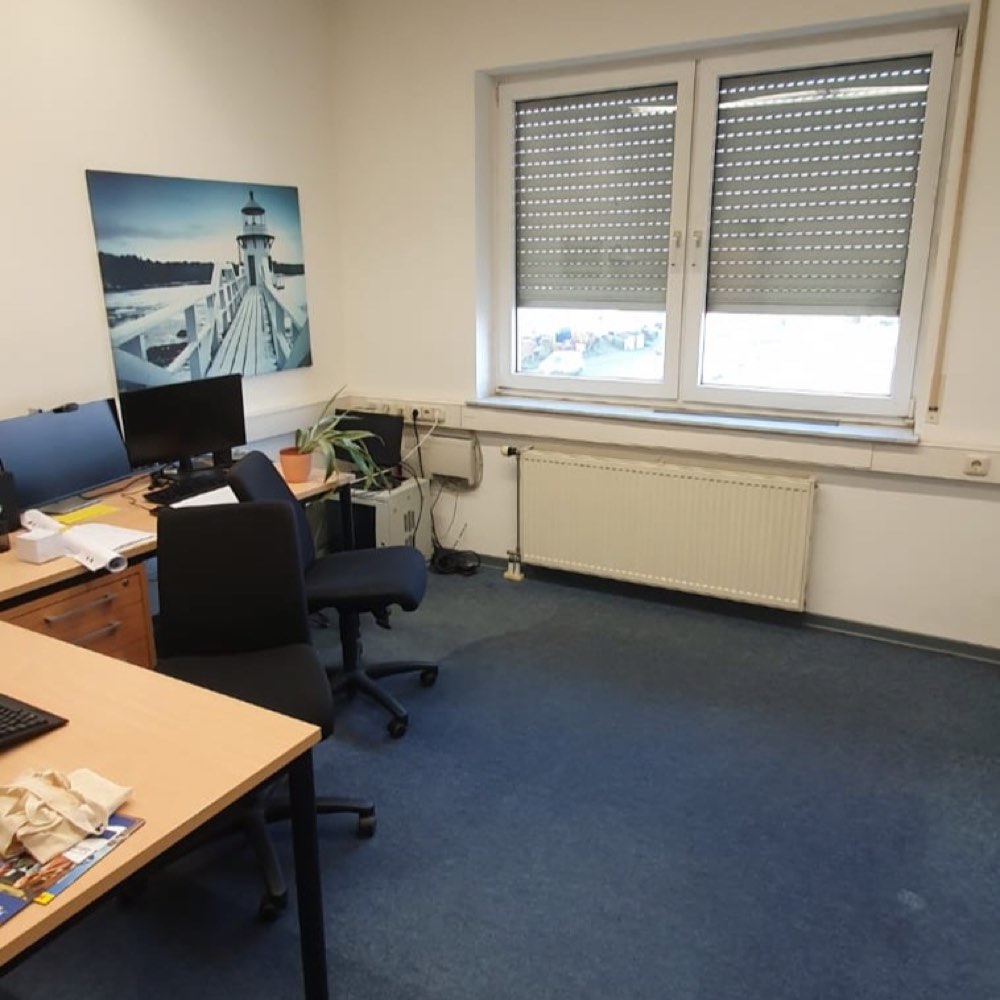 Büro im laufenden Betrieb mit Schreibtischen, Bildschirmen und blauem Teppichboden